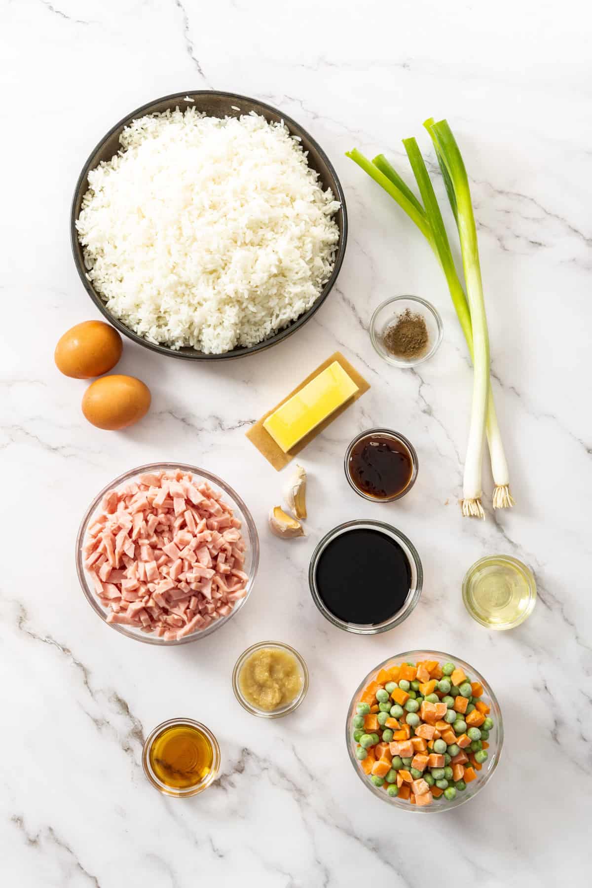 a bowl of rice, veggies, chopped ham, butter, and other ingredients on a white marble background.