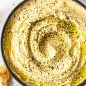 homemade hummus in a black bowl topped with seeds and olive oil.
