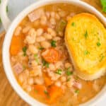 a white bowl with handles filled with ham and beans and topped with a slice of bread.