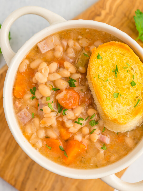 a white bowl with handles filled with ham and beans and topped with a slice of bread.