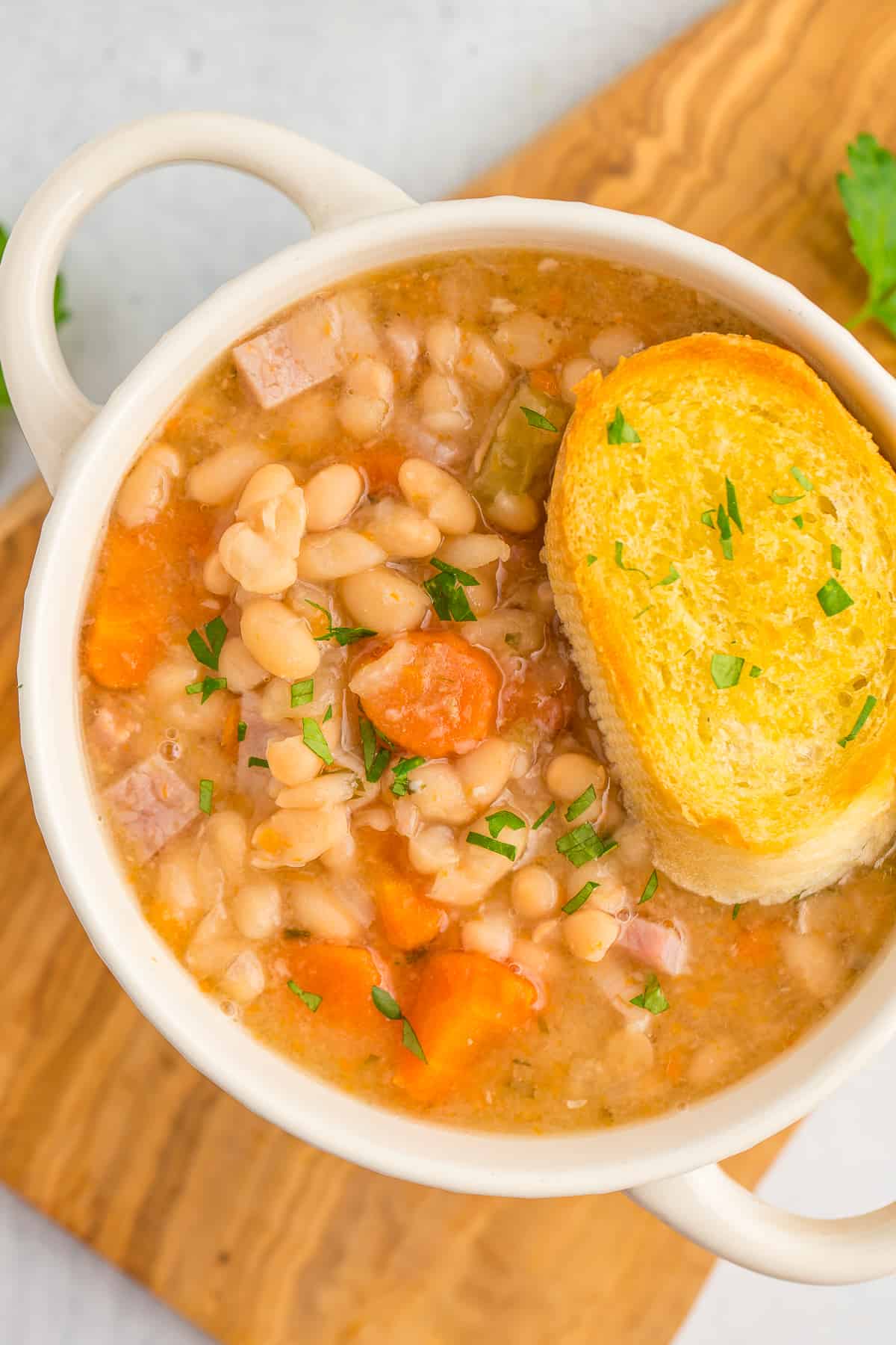 a white bowl with handles filled with ham and beans and topped with a slice of bread.