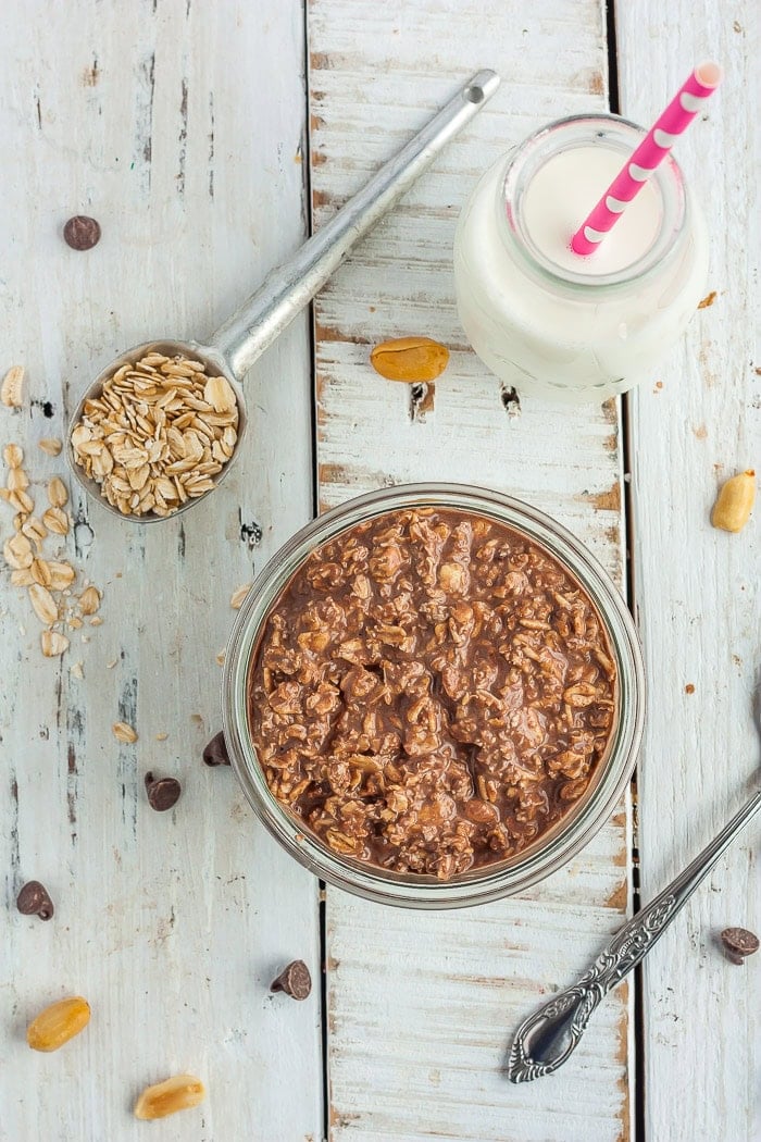 a glass jar with chocolate overnight oats on a white board with a small bottle of milk.