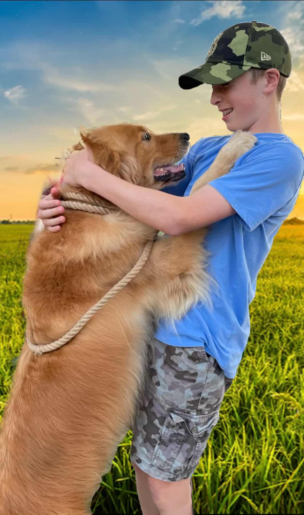 a teen in a camo hat with a dog hugging him