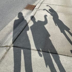the shadows of 3 people on a sidewalk.