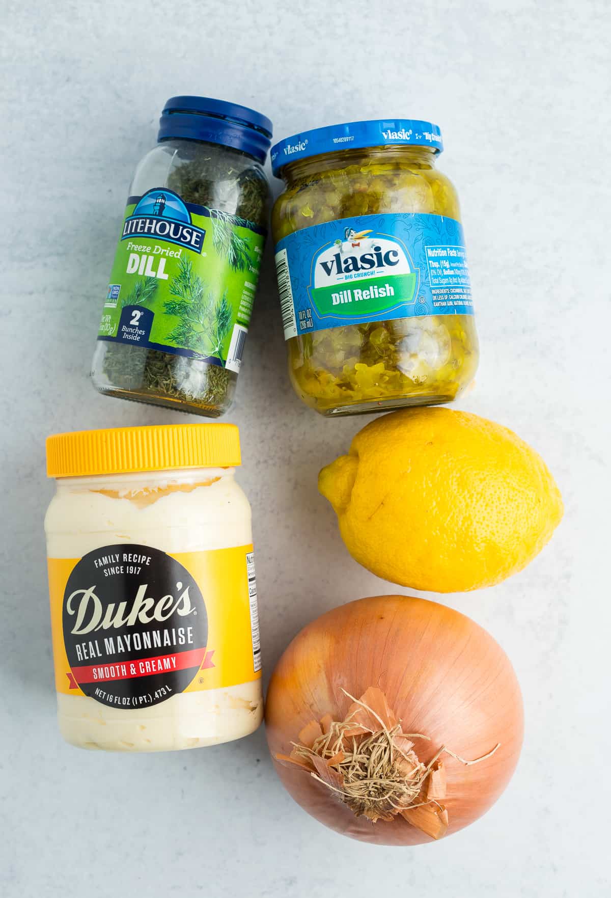 Mayonnaise, Dill, Zwiebel, Zitrone und Dill-Relish auf einer weißen Tafel.