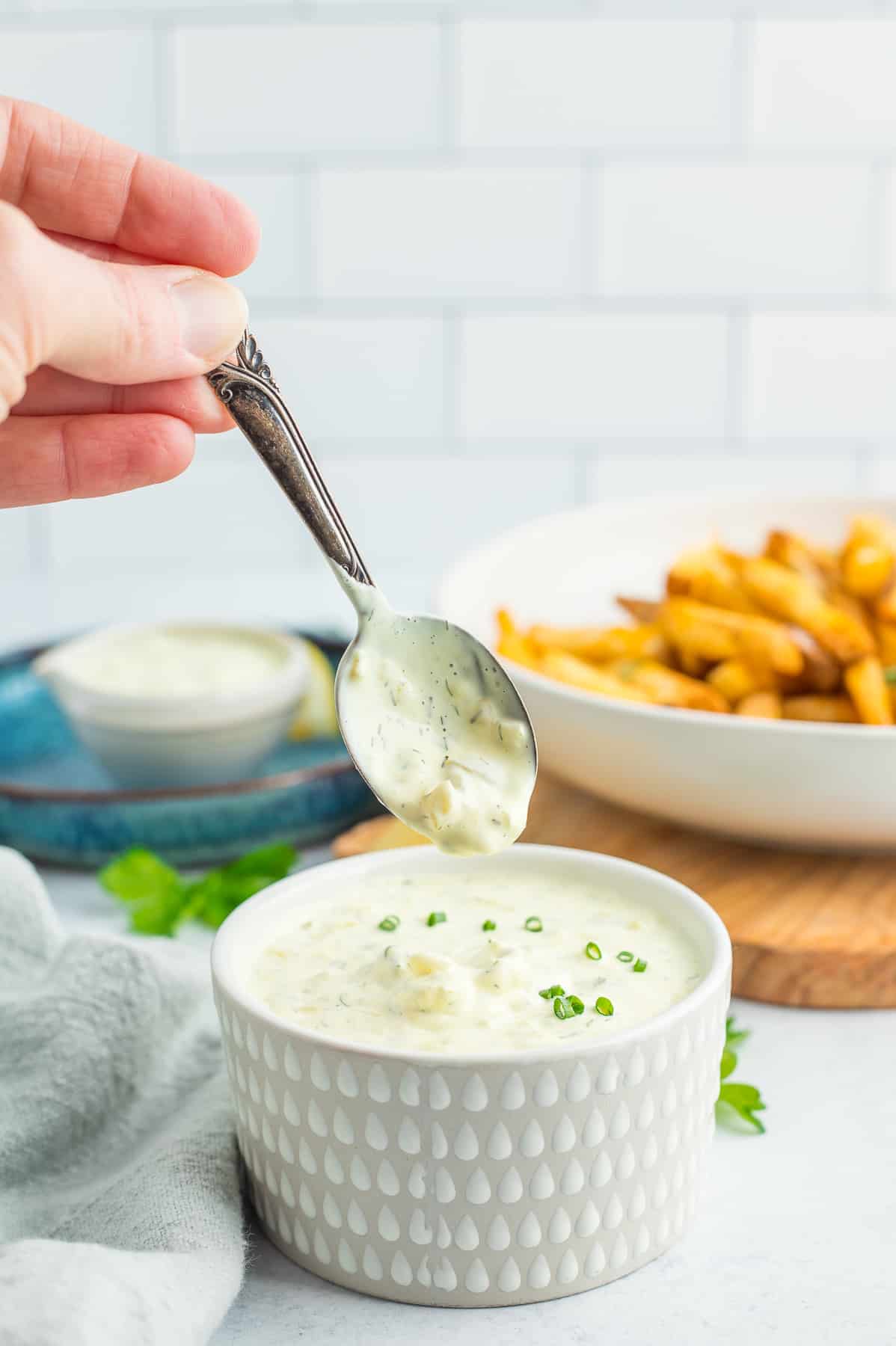 a spoon hovering over a bowl of dill aioli.