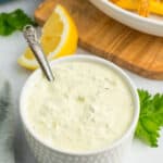 a white textured dish filled with homemade tartar sauce with a small bronze spoon in it.