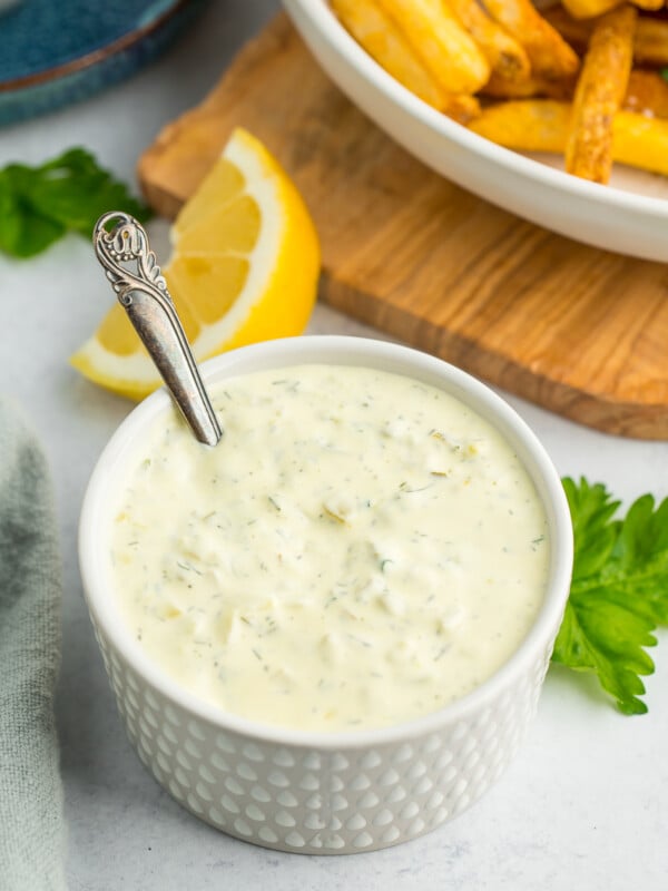 a white textured dish filled with homemade tartar sauce with a small bronze spoon in it.