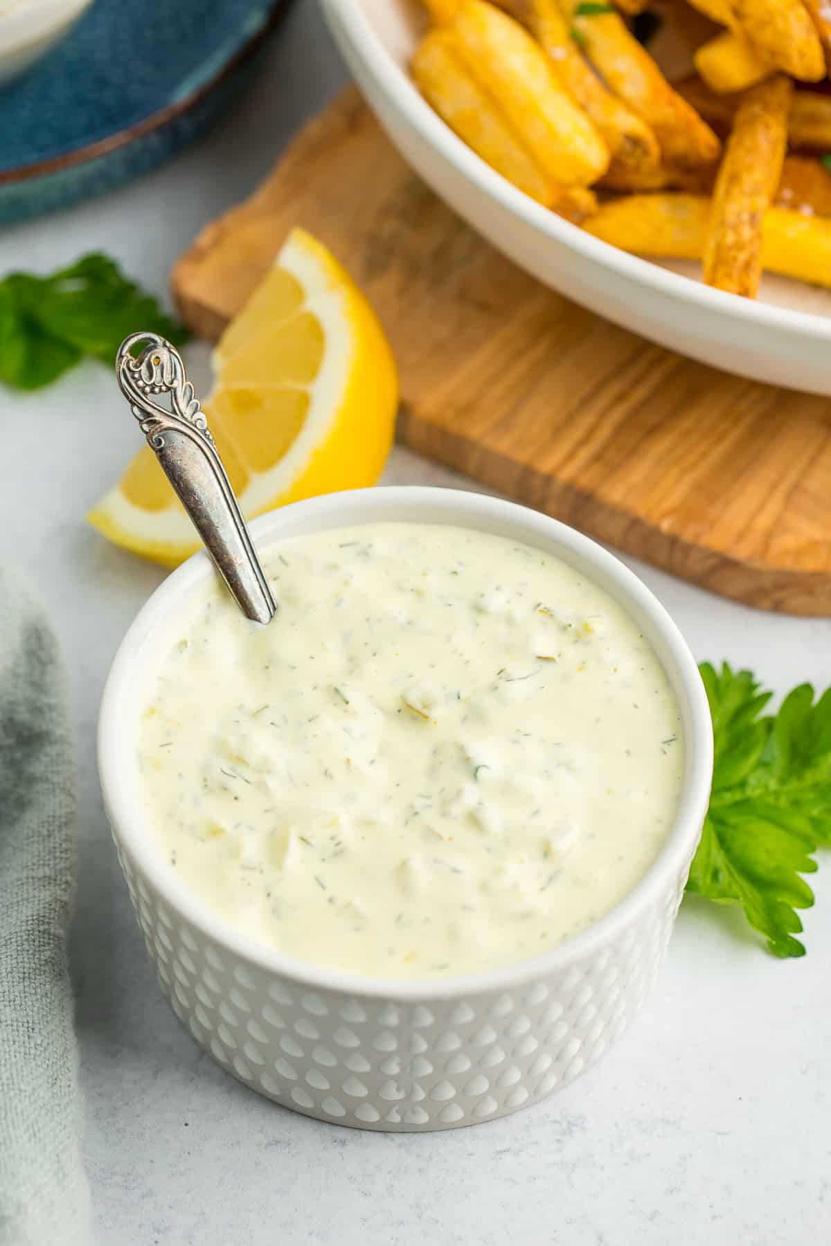 a white textured dish filled with homemade tartar sauce with a small bronze spoon in it.