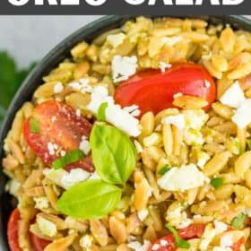 a blue bowl with pesto orzo and tomatoes topped with fresh basil and feta.