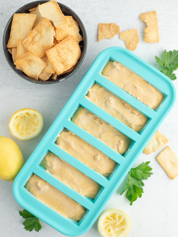 a teal freezer tray with hummus on a white board with a bowl of chips, lemons, and parsley.