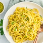 a white bowl with creamy pesto pasta topped with chopped parsley.