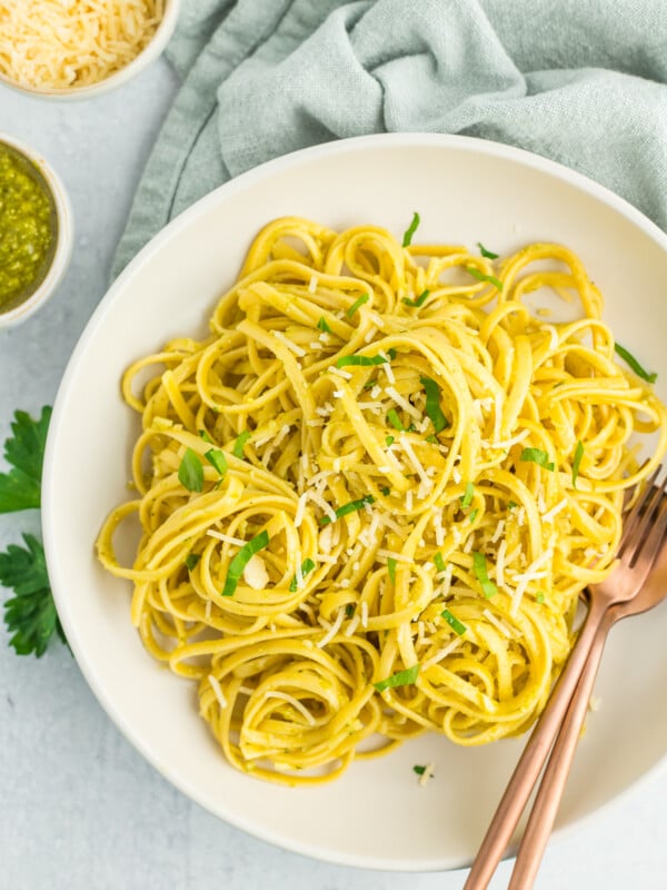 a white bowl with creamy pesto pasta topped with chopped parsley.
