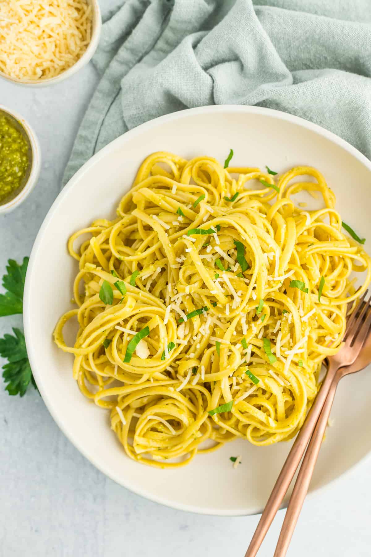 a white bowl with creamy pesto pasta topped with chopped parsley.