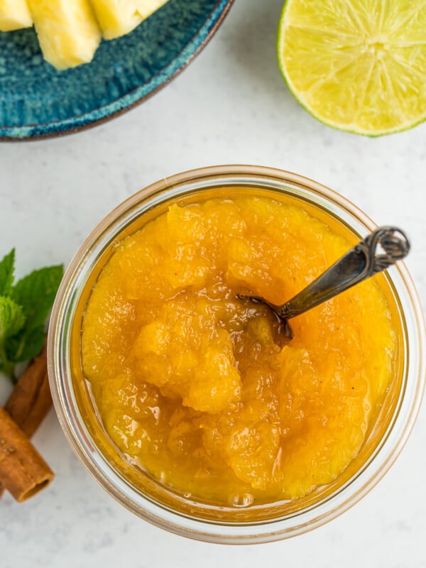 a glass dish of pineapple jam with a small bronze spoon in it.