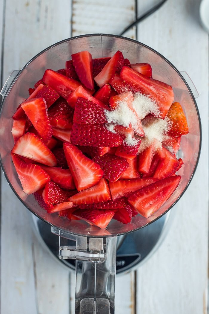 a food processor with sliced fruit and sugar.