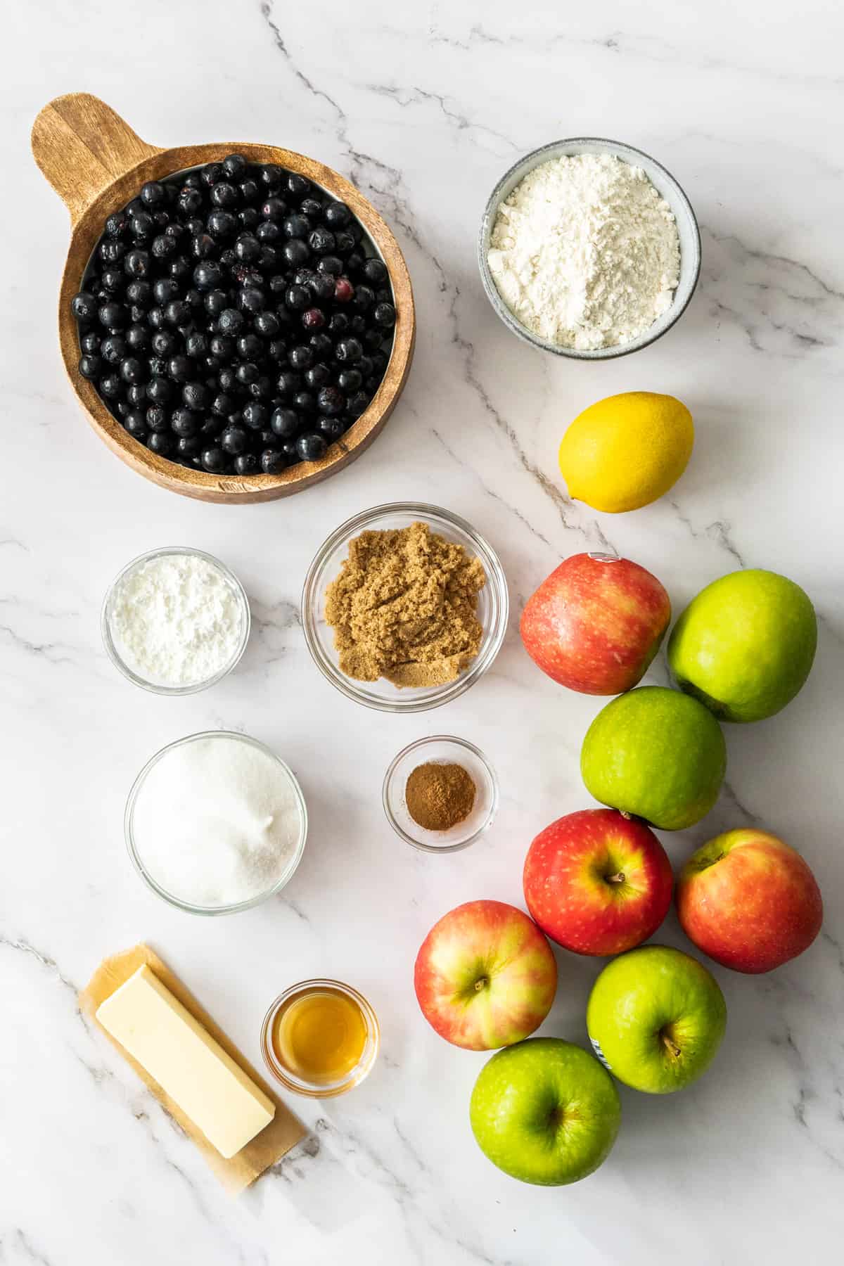 apples, blueberries, butter, flour, and other ingredients on a white board.