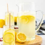 a pitcher and glasses of lemonade with sliced lemons on a board.