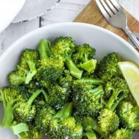 steamed broccoli in a white bowl topped with flaky salt and a lemon slice.