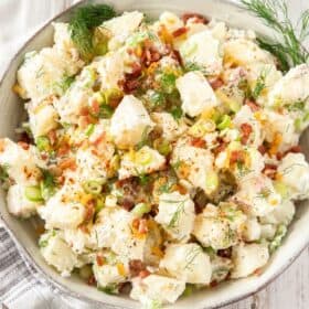 baked potato salad in a white bowl topped with bacon and fresh dill.
