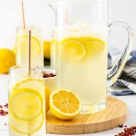 a pitcher and glasses of lemonade with sliced lemons on a board.