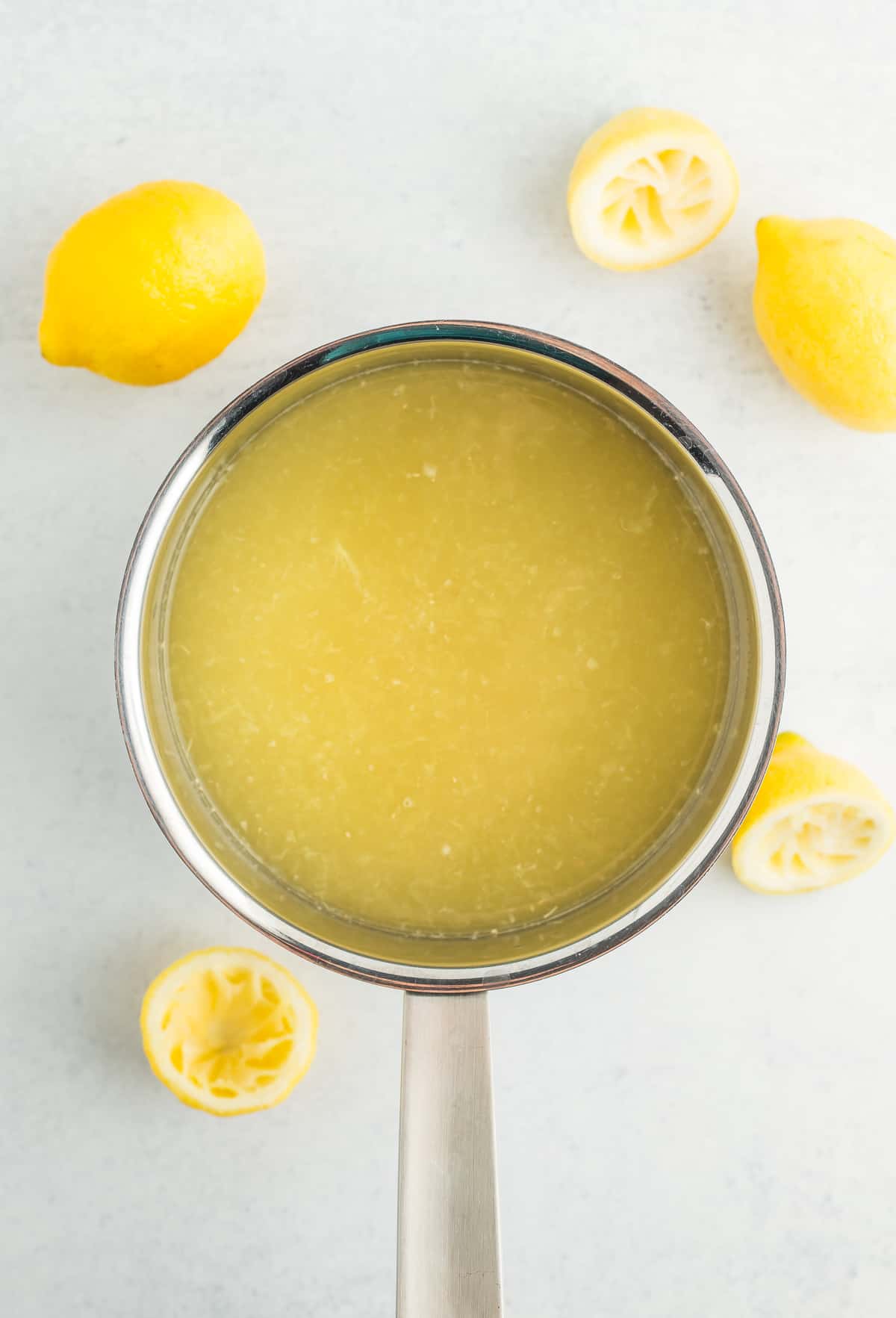lemon juice and sugar in a saucepan with fresh lemons surrounding it.