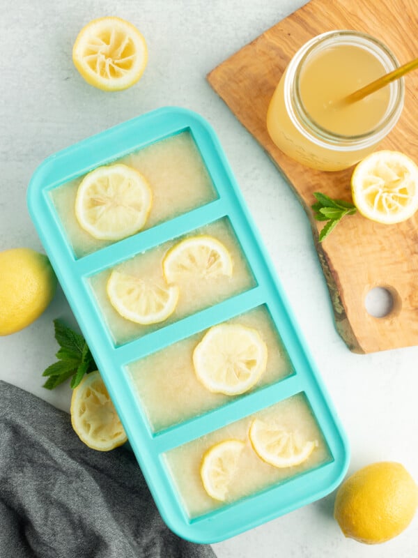 frozen blocks of lemonade concentrate with sliced lemons on top an a glass with a straw.