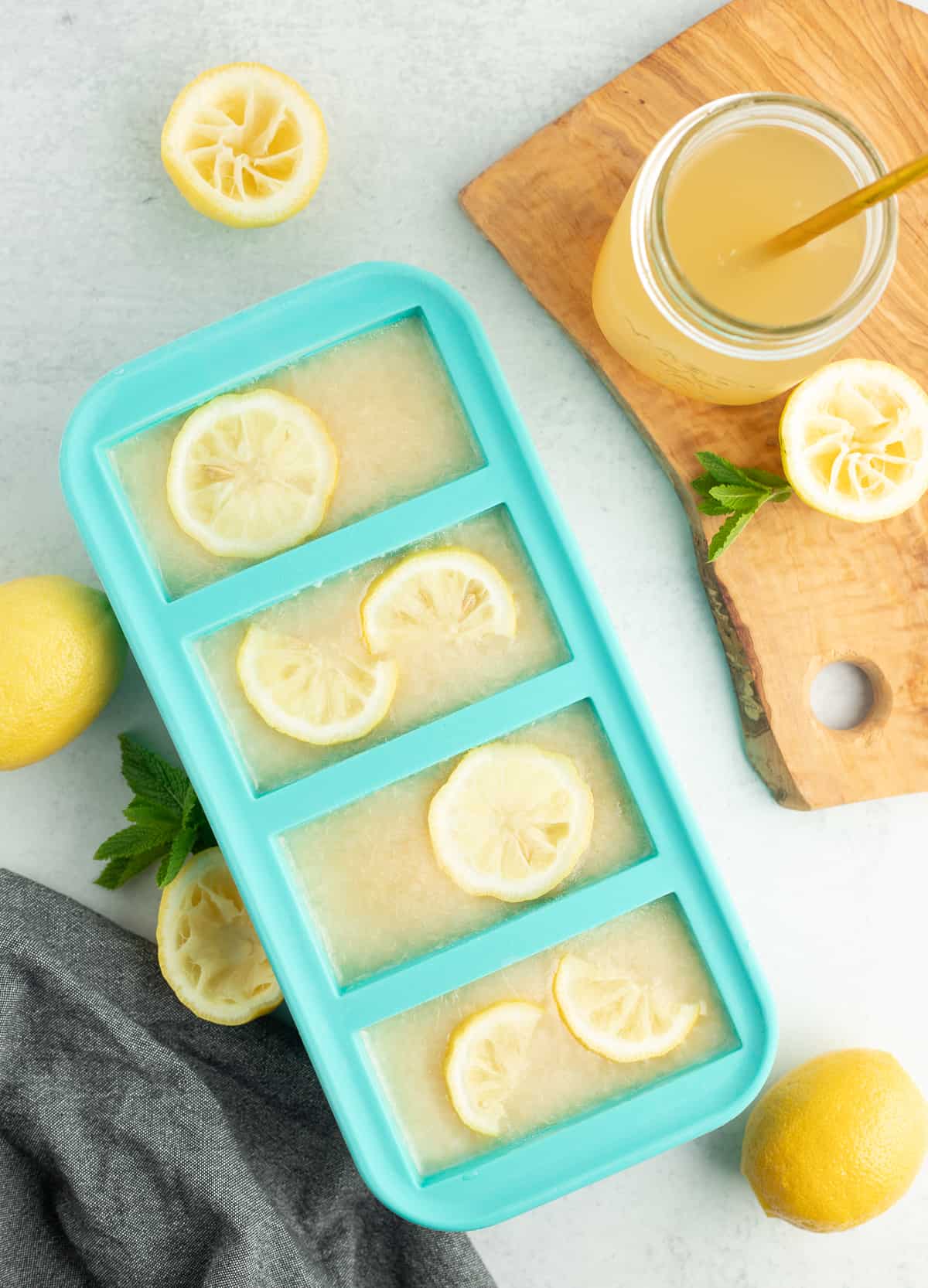 frozen blocks of lemonade concentrate with sliced lemons on top an a glass with a straw.