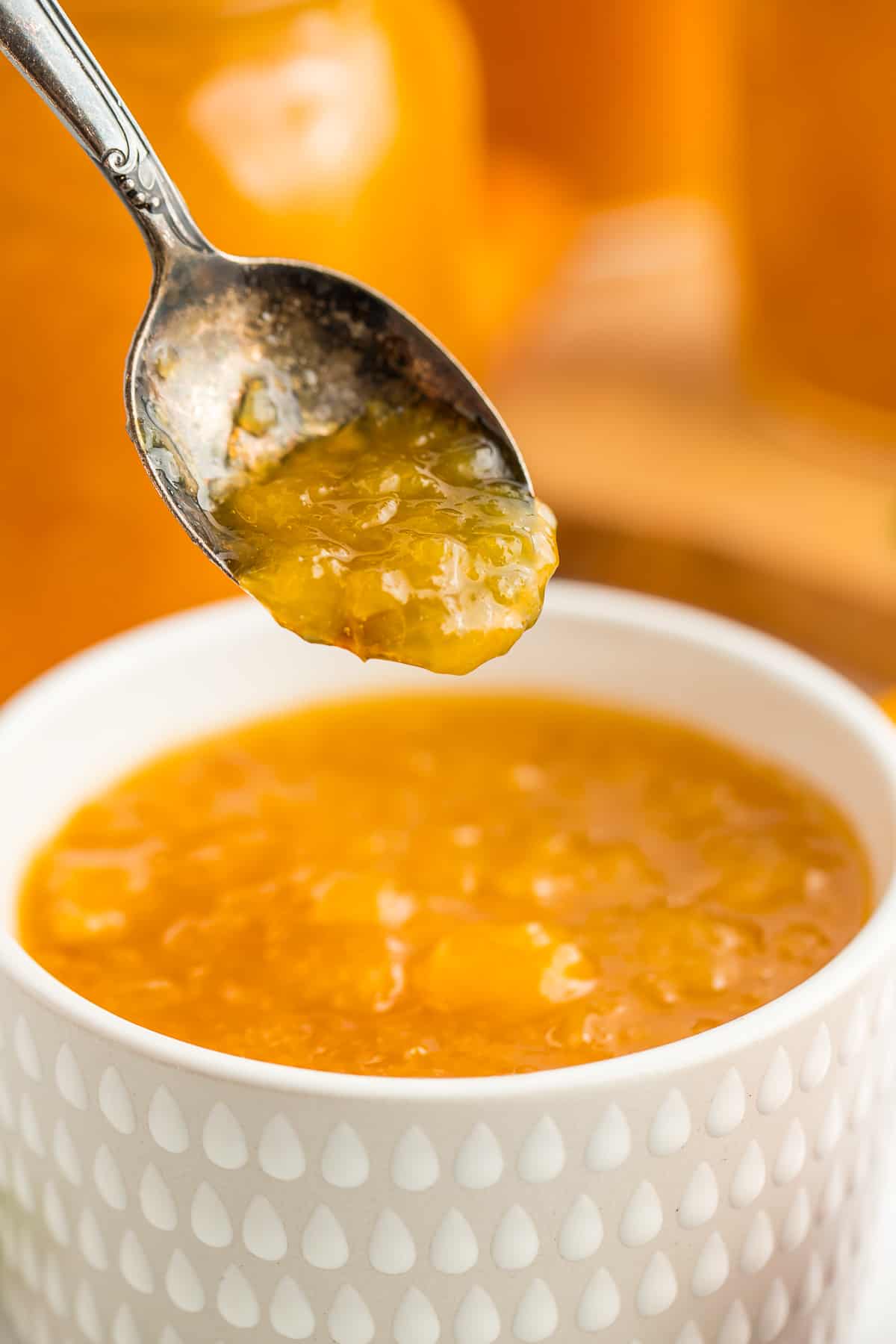 a white bowl of peach preserves with a spoonful hovering over it.