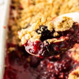 a white dish of blackberry apple crumble on a wooden board.