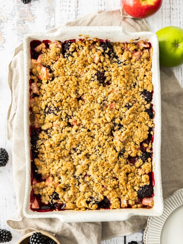 a white dish of blackberry apple crumble on a wooden board.