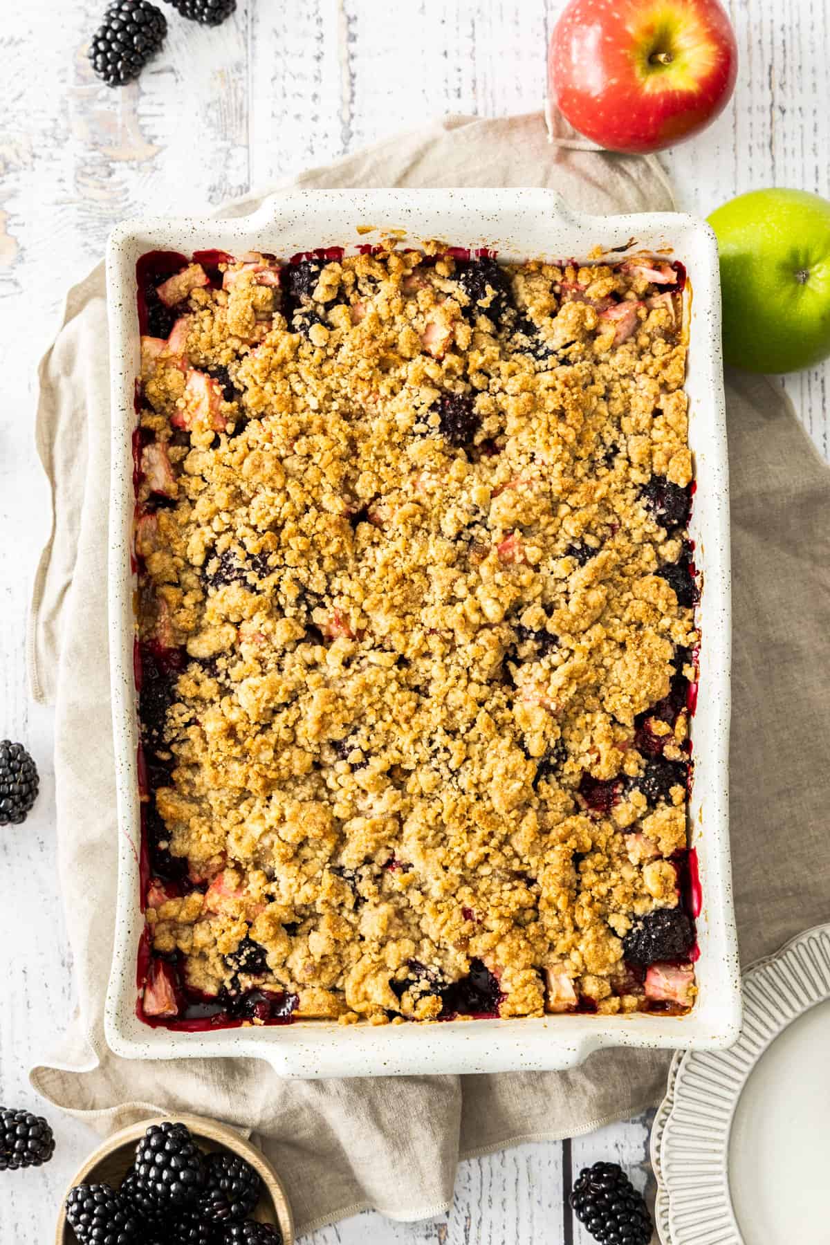 a white dish of blackberry apple crumble on a wooden board.