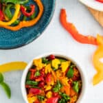 A white dish full of dried peppers with other pepper slices on a blue plate and a white board.