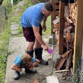a boy and his dad both in blue shirts and boots in front of a woodshed.