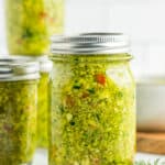 3 jars of zucchini relish on a marble board with a tile background.