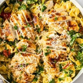 a white skillet with creamy chicken pesto pasta topped with shredded parmesan.