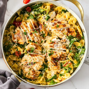 a white skillet with creamy chicken pesto pasta topped with shredded parmesan.