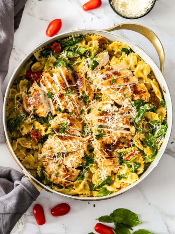 a white skillet with creamy chicken pesto pasta topped with shredded parmesan.