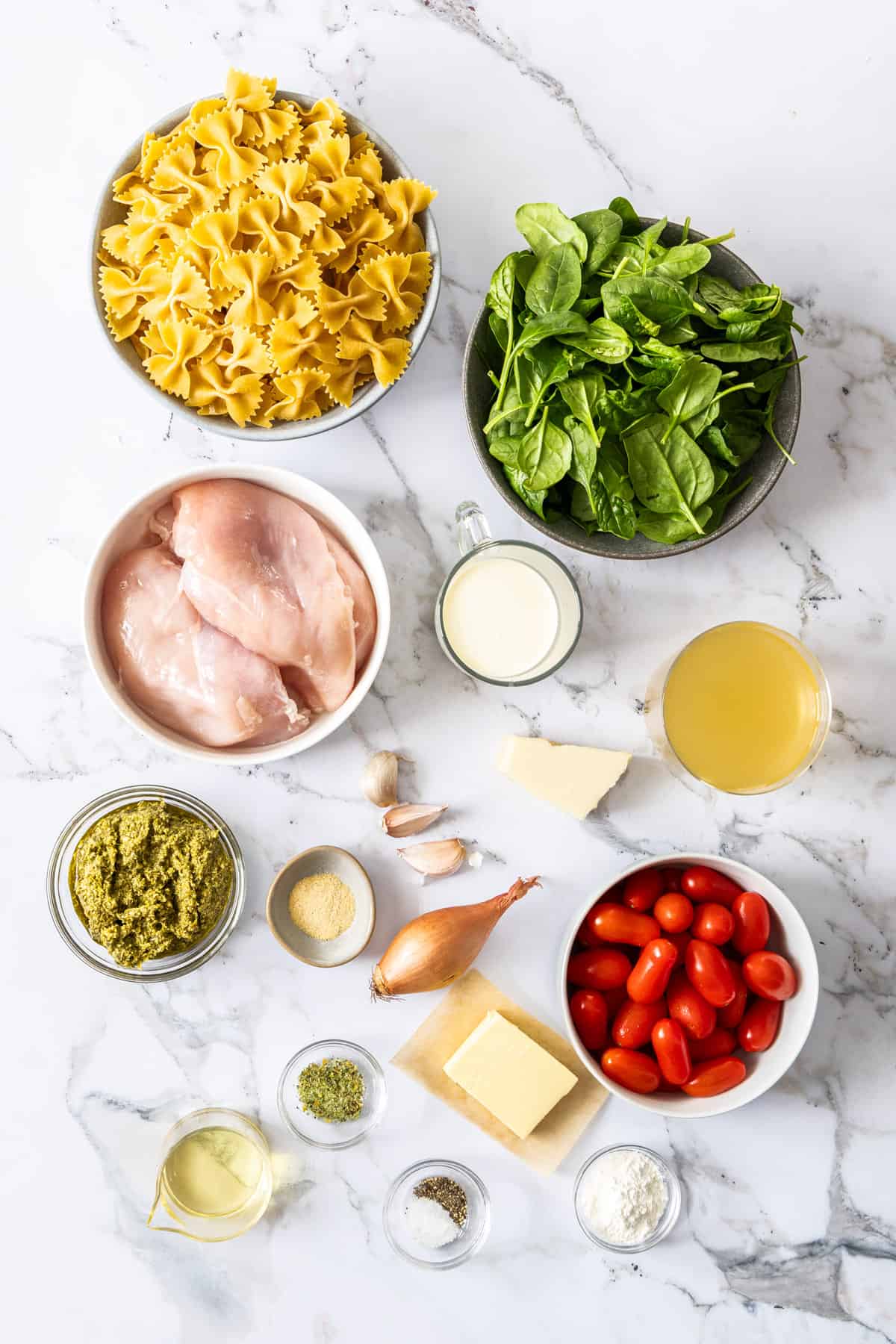 a bowl of chicken, noodles, spinach, tomatoes, and other ingredients on a marble board.