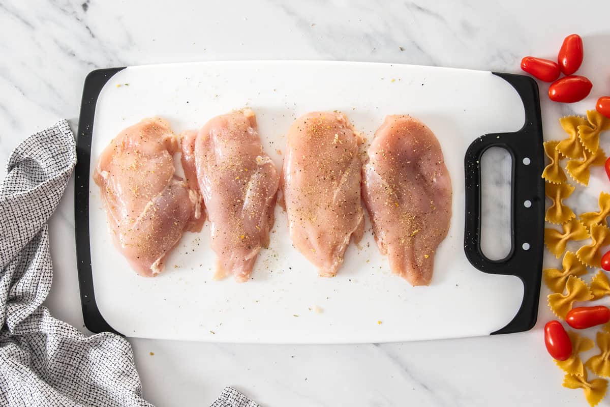 4 chicken breasts on a cutting board topped with salt and pepper.