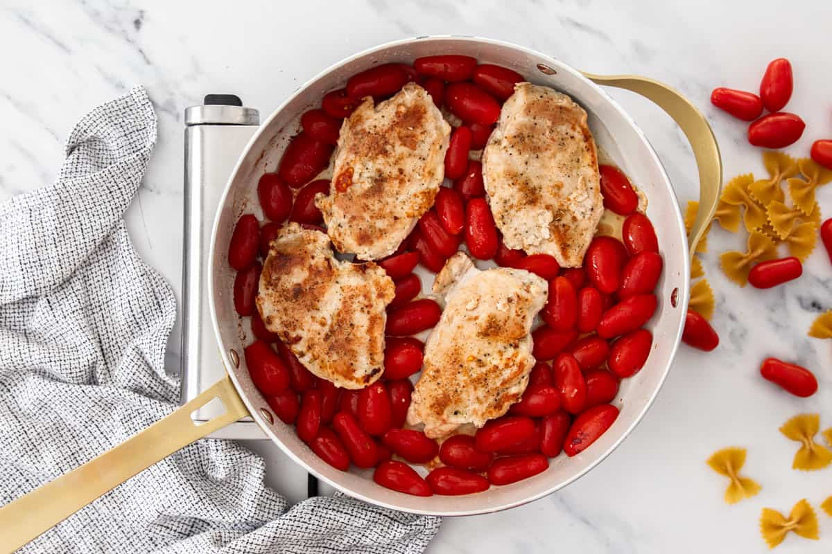 sliced tomatoes and whole chicken breasts in a white skillet.