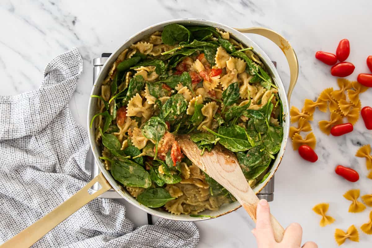chicken and noodles with baby spinach in a white skillet.