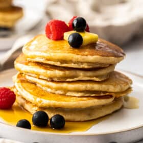 a stack of whole wheat pancakes topped with butter and berries with a small puddle of maple syrup on the plate.