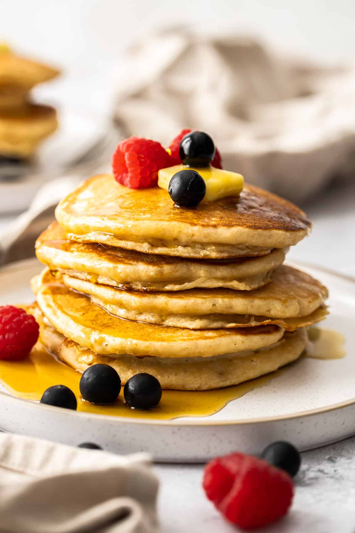 a stack of whole wheat pancakes topped with butter and berries with a small puddle of maple syrup on the plate.
