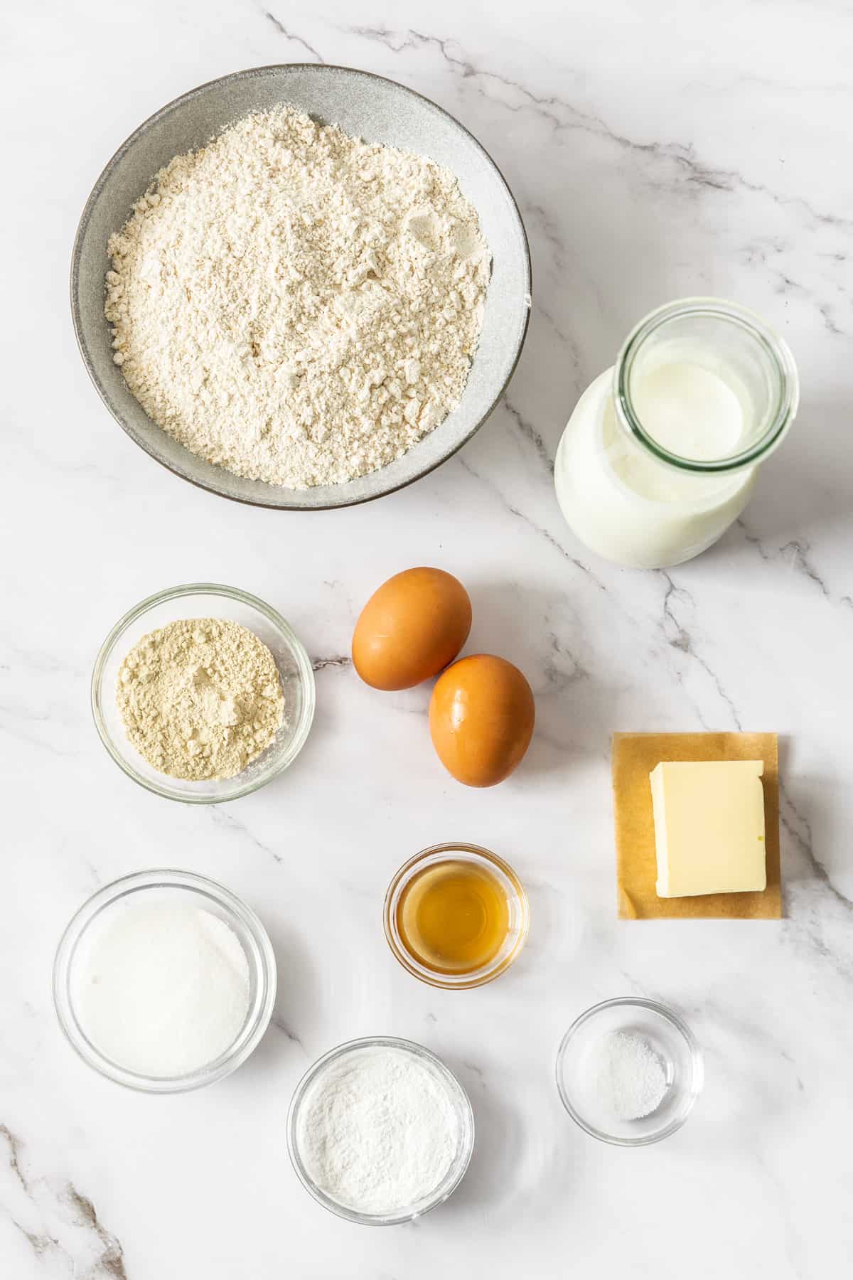 bowls of whole wheat, sugar, baking soda, eggs, milk, butter, and other ingredients on a marble board.