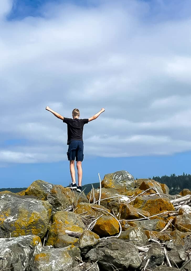 a kid standing on rocks with his arms in the air.