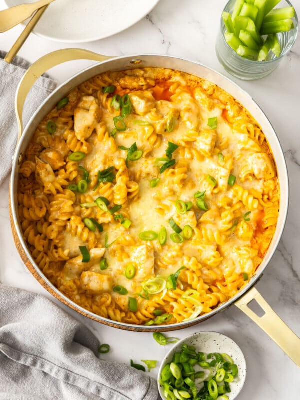 a white dish with buffalo chicken casserole topped with sliced green onions.