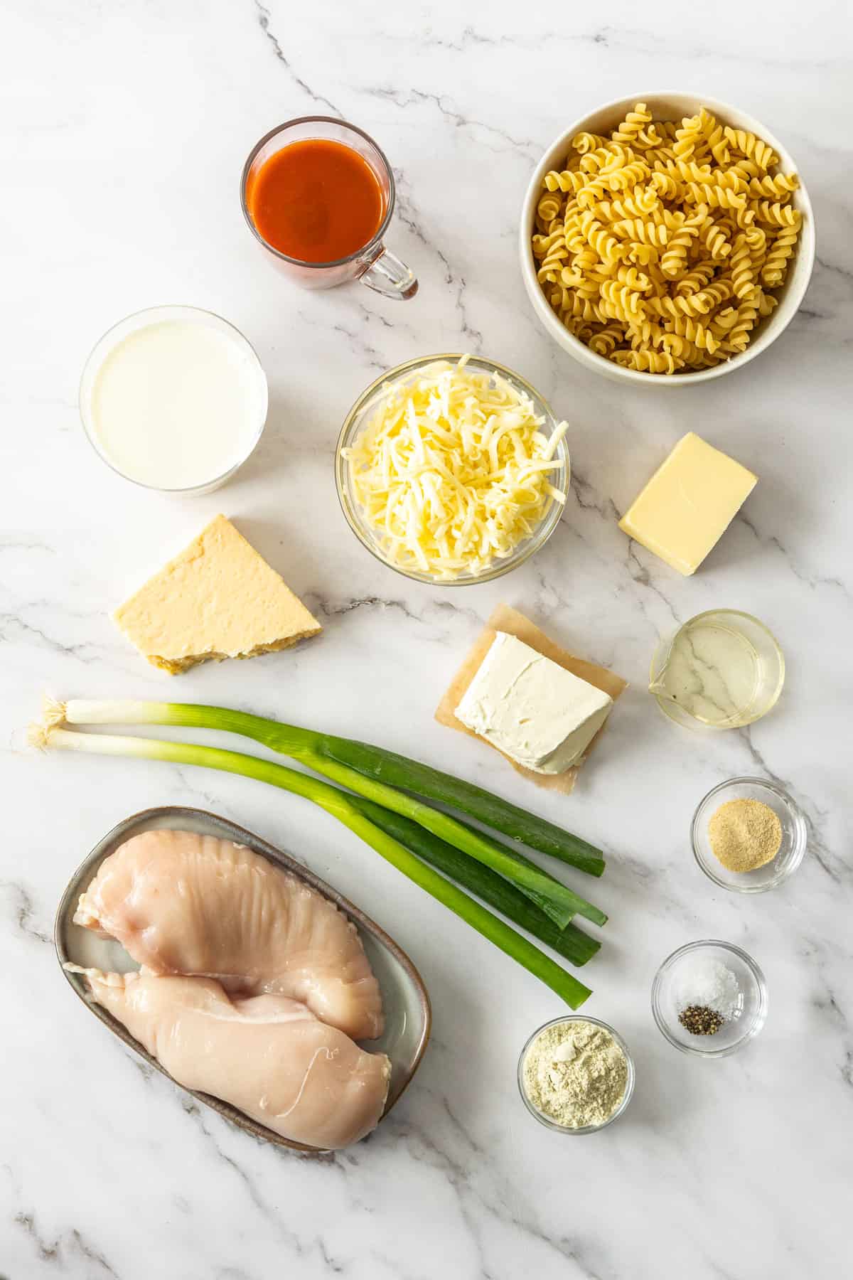 a bowl of rotini, cheese, chicken, and other ingredients on a white marbled board.