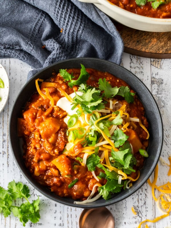 a dark grey bowl filled with butternut squash chili topped with sour cream, cilantro, and shredded cheese.