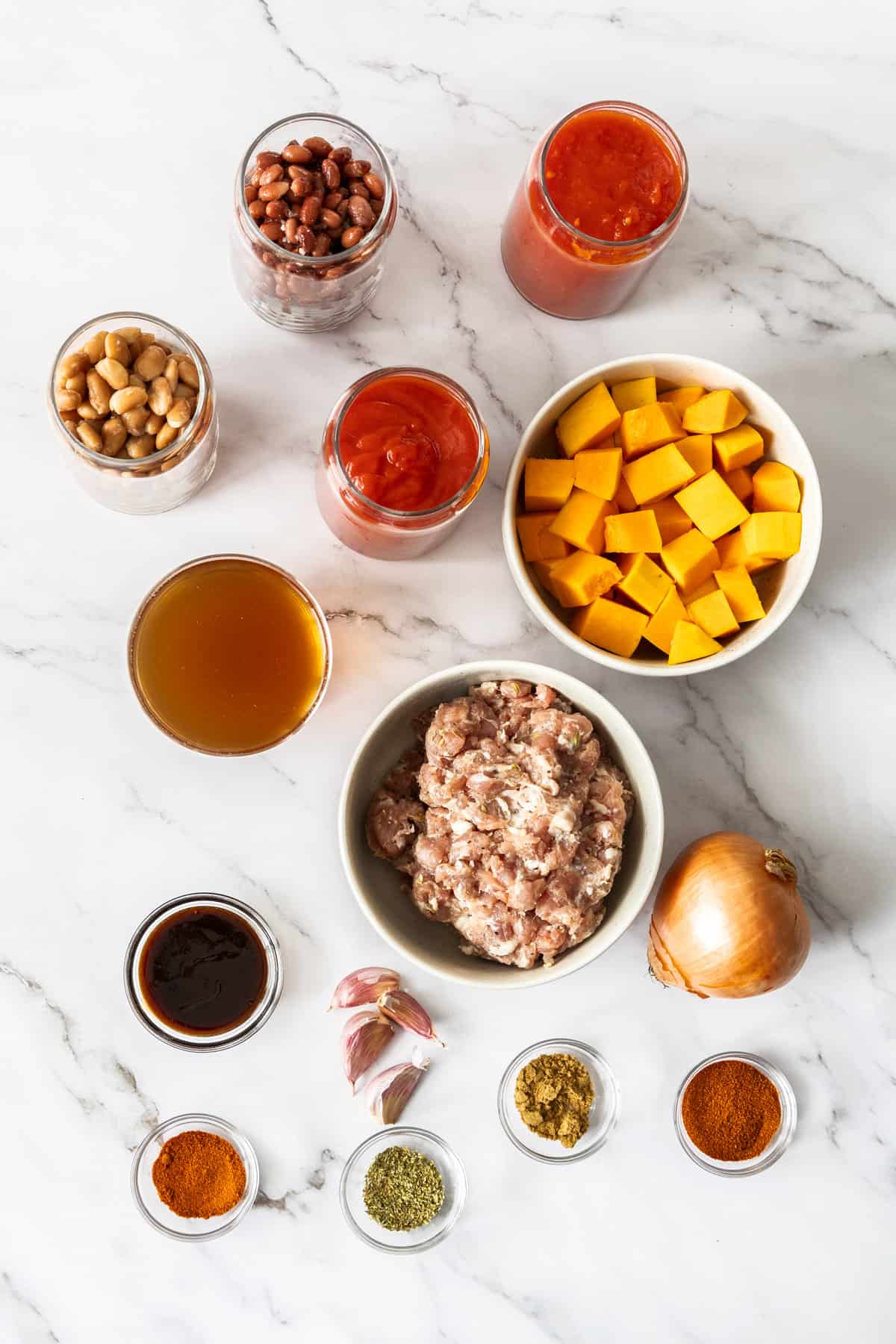 bowls of ground sausage, butternut squash, seasonings, and other ingredients on a marbled board.